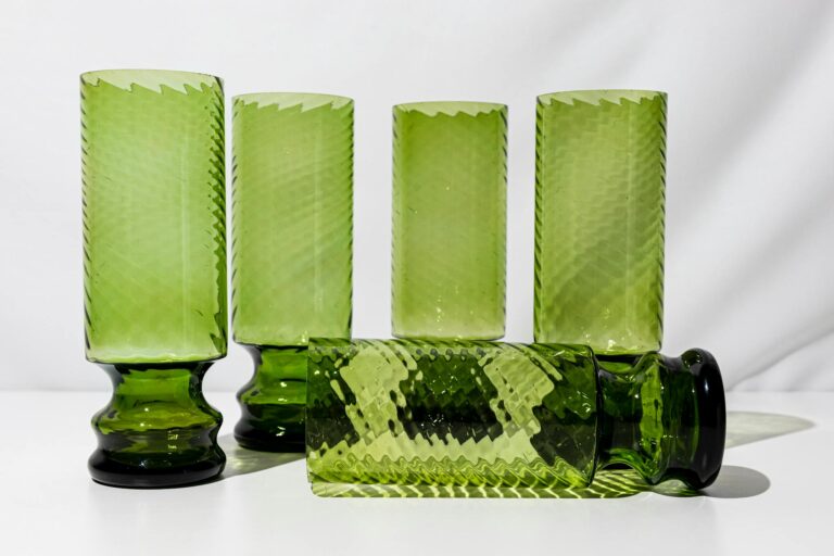 A set of vintage green glass tumblers with textured patterns arranged on a white surface.
